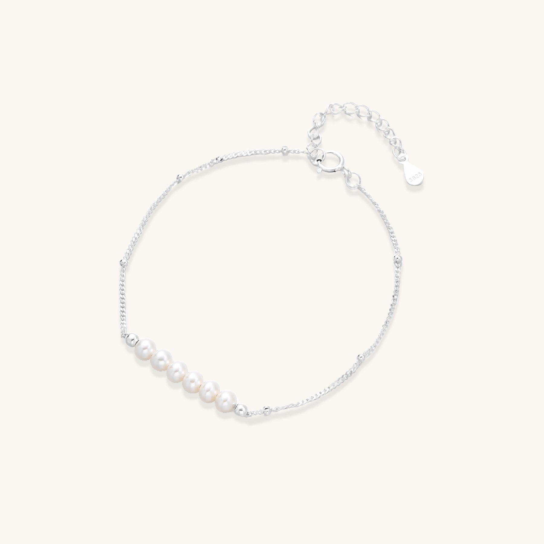 Dainty sterling silver bracelet with small white baroque pearls and adjustable chain on neutral background.