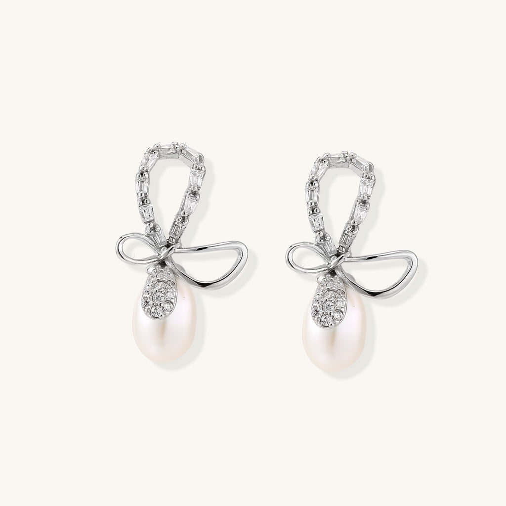 Sterling silver stud earrings with baguette crystal bow design and freshwater pearl drops on white background