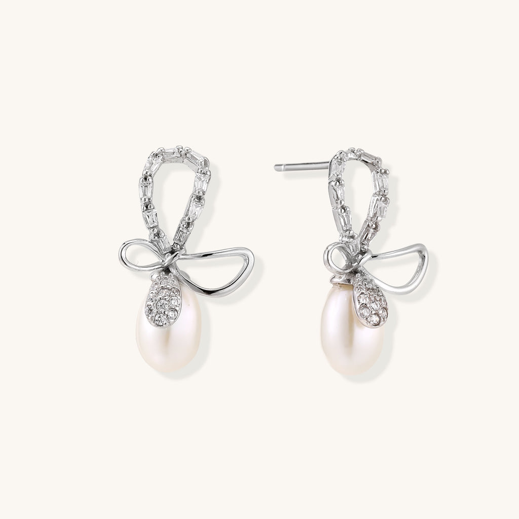 Sterling silver stud earrings with baguette crystal bow design and freshwater pearl drops on white background