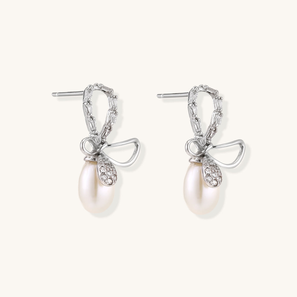 Sterling silver stud earrings with baguette crystal bow design and freshwater pearl drops on white background