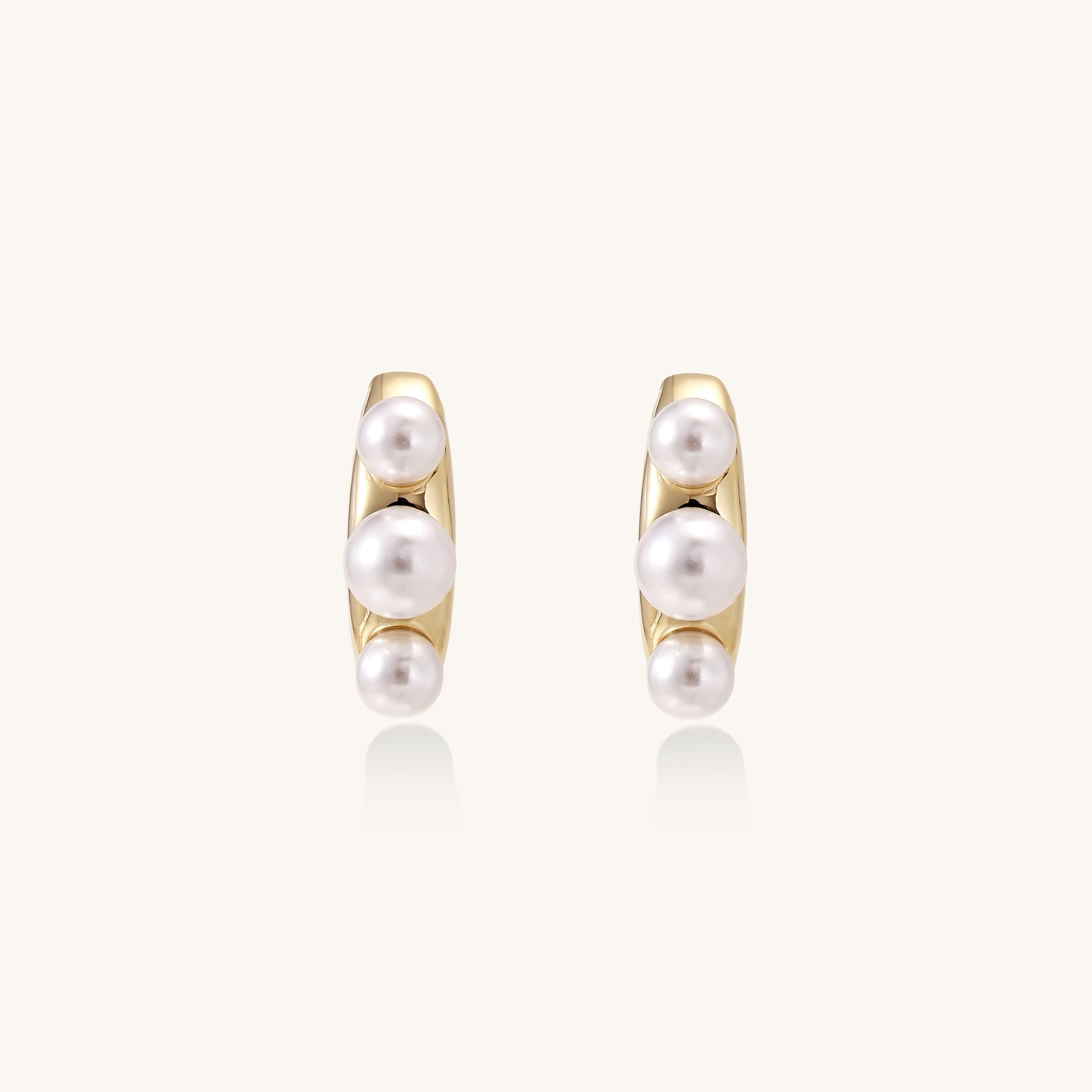 Delicate gold stud earrings with three lustrous white freshwater pearls arranged in an organic curved line.