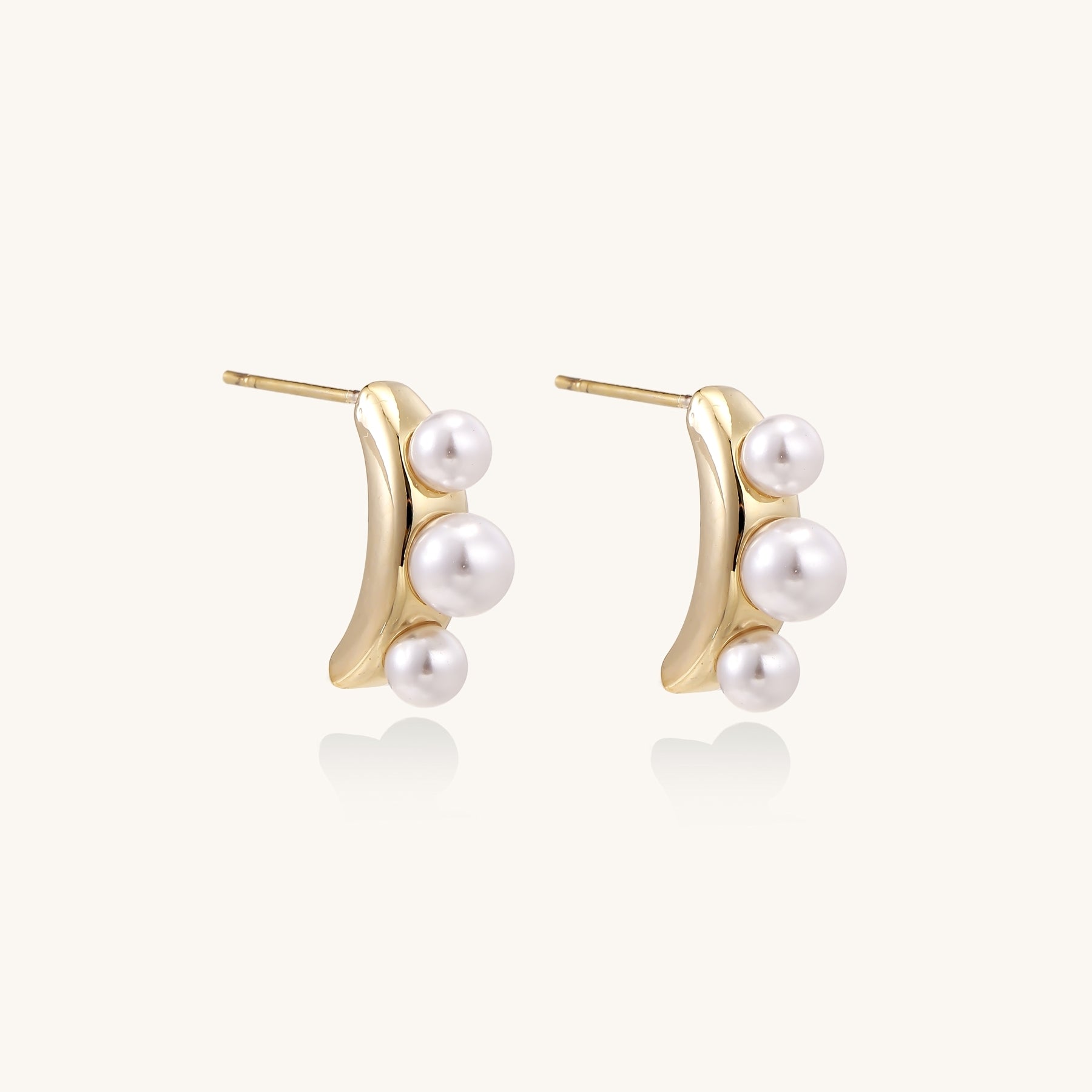 Delicate gold stud earrings with three lustrous white freshwater pearls arranged in an organic curved line.