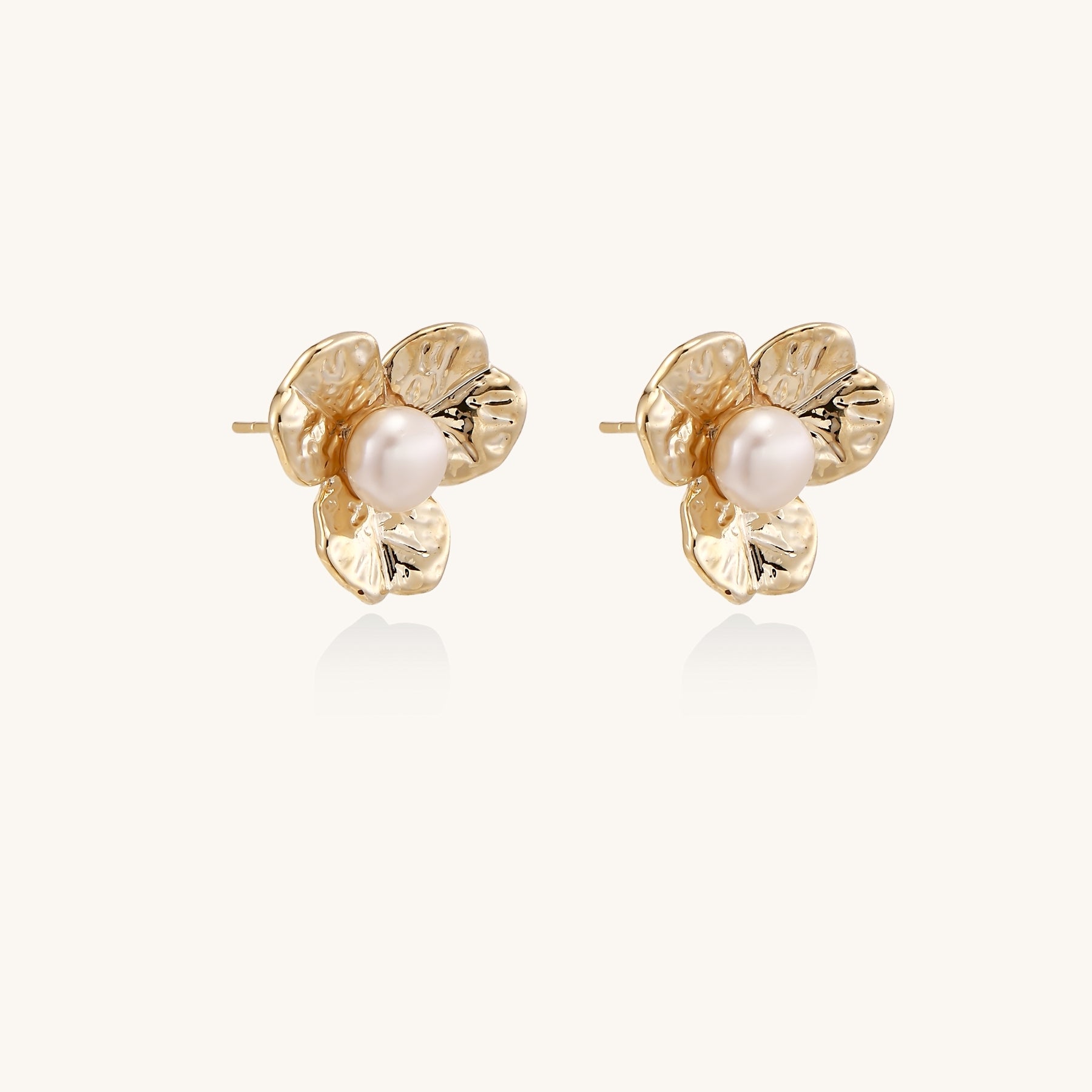 Gold-plated flower stud earrings with freshwater pearl centers on beige background, showing textured petal details.