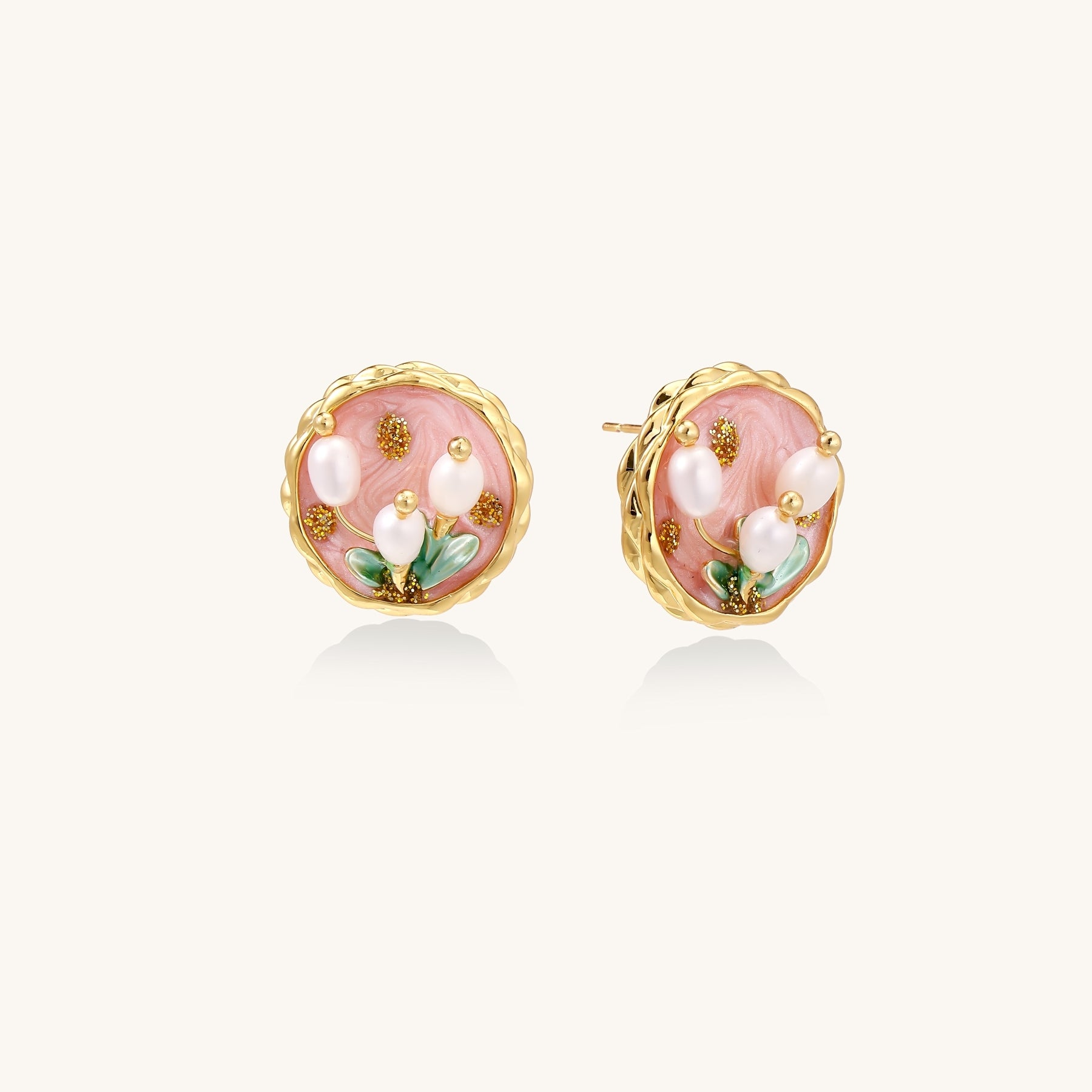 Round stud earrings with pink enamel background, white pearl tulips, green leaves, and twisted gold border on white background.