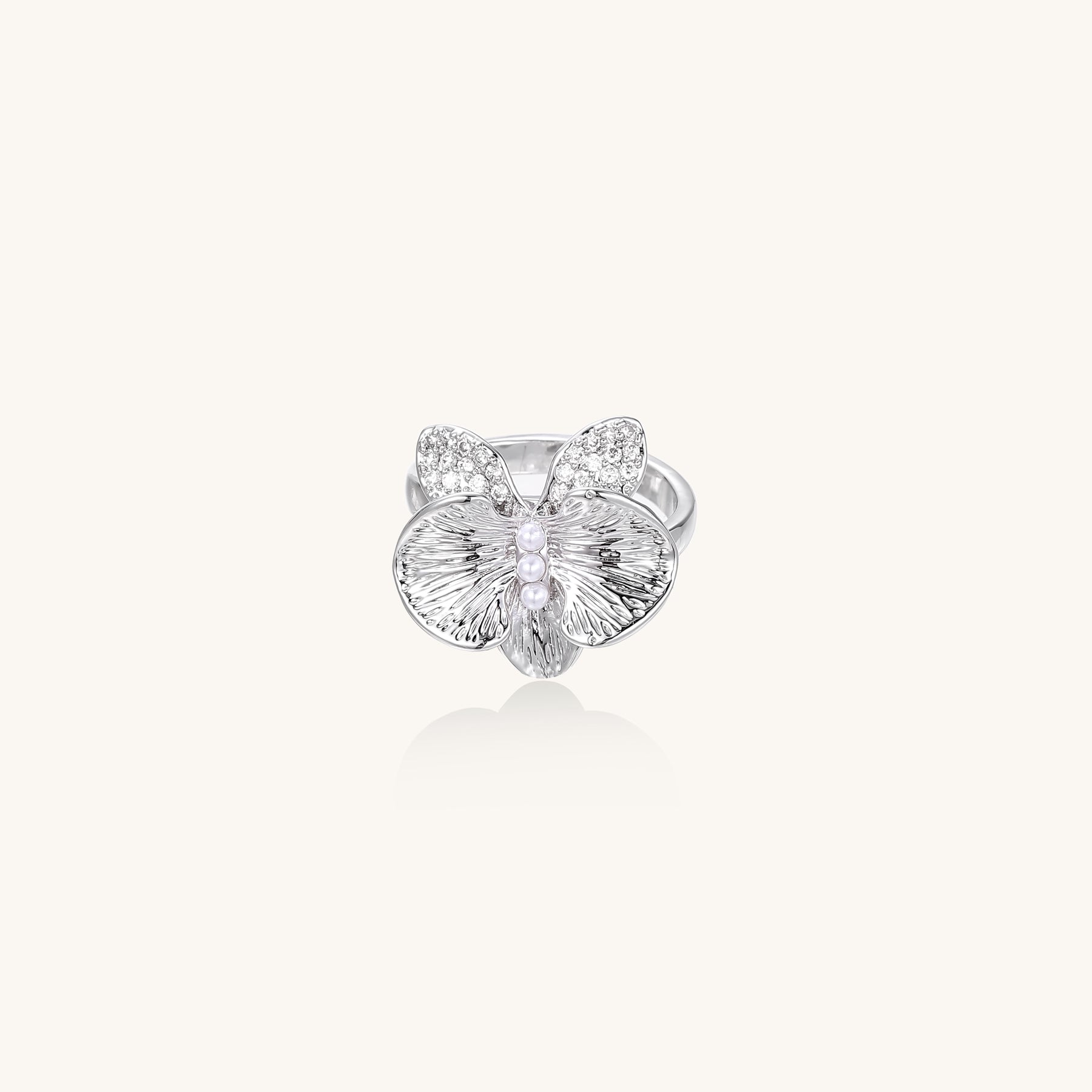 Gold-plated brass ring with textured orchid petals, zirconia stones, and center pearls on white background.