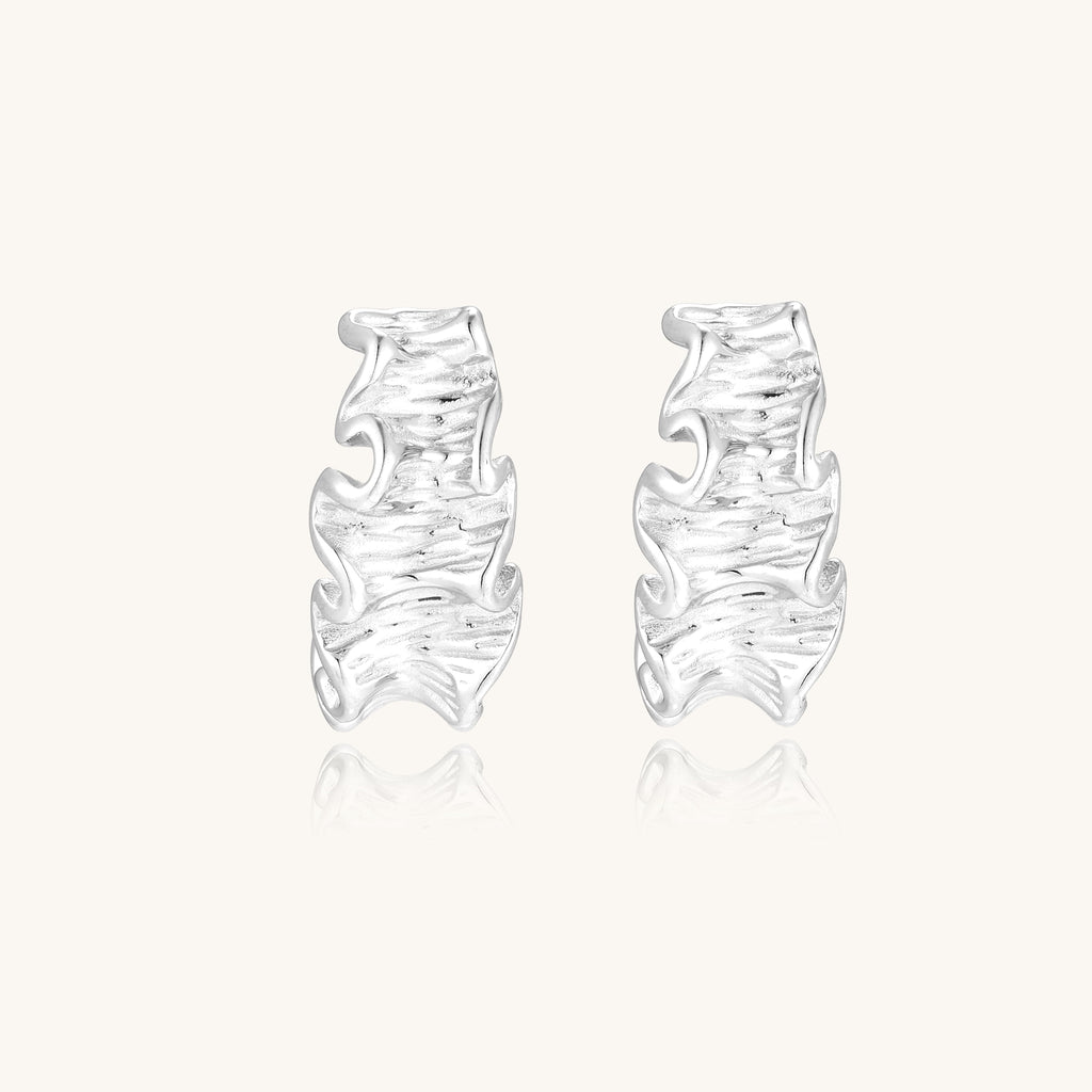 Textured gold-plated hoop earrings with flowing ripple design displayed on clean white background.