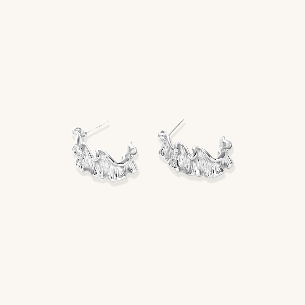 Textured gold-plated hoop earrings with flowing ripple design displayed on clean white background.