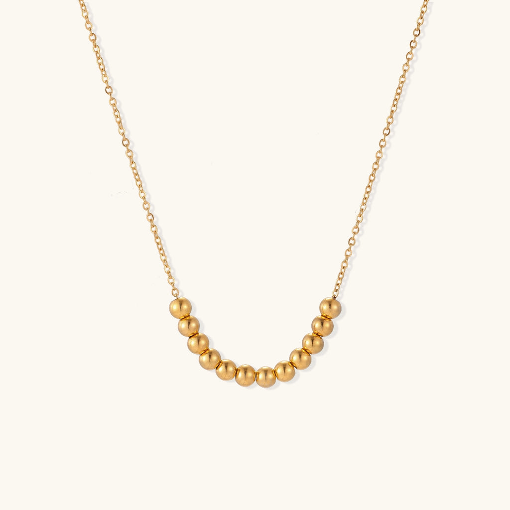 Delicate gold-plated chain necklace featuring clustered spherical beads arranged in elegant curve against white background.