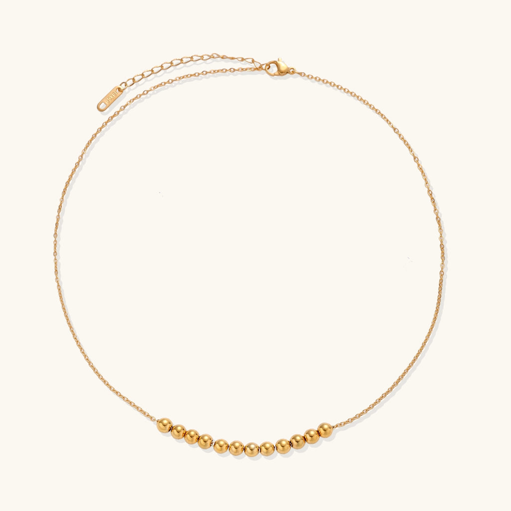 Delicate gold-plated chain necklace featuring clustered spherical beads arranged in elegant curve against white background.