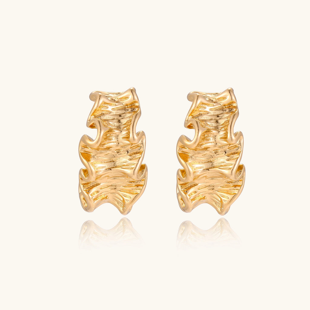 Close-up of dimensional gold-plated hoop earrings with rippled wave texture against white background.