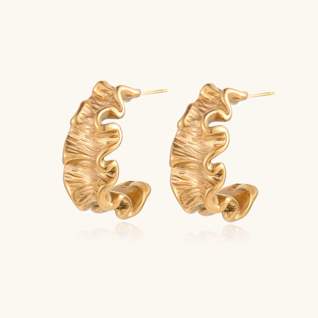 Textured gold-plated hoop earrings with wavy sculptural ridges displayed against a neutral background.
